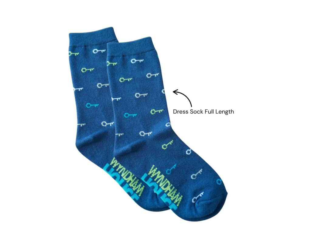Shows the design of the navy dress sock for the Wyndham House socks for shelter campaign. The sock design is a navy sock with a blue, green and white key pattern.